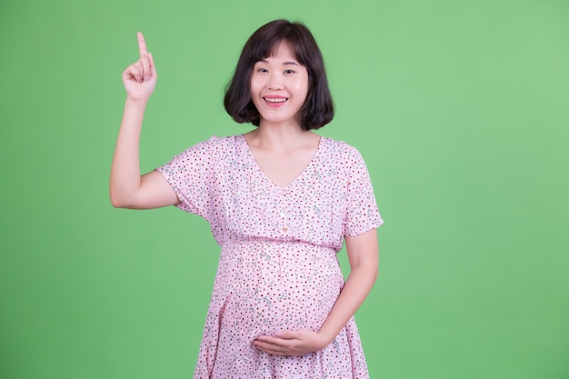 Retrato de uma linda mulher asiática grávida com cabelo curto contra chroma key ou parede verde