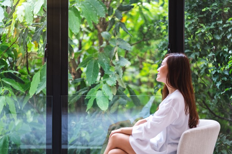 Foto retrato de uma linda mulher asiática sentado e olhando para uma natureza verde fora da janela