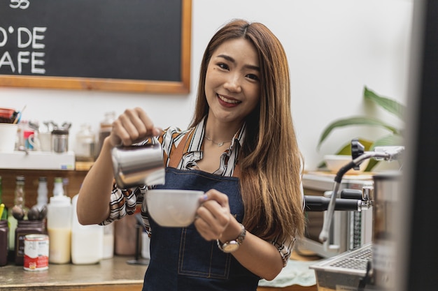 Retrato de uma linda mulher asiática servindo leite para fazer latte art para um cliente, ela é dona de uma cafeteria, o conceito de uma empresa de alimentos e bebidas. gestão de loja por uma mulher de negócios.