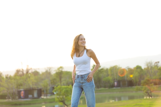 Retrato de uma linda mulher caucasiana, sorrindo e olhando para o parque. Jovem feliz no pôr do sol na natureza com as mãos abertas