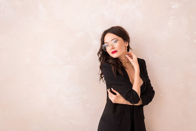 Foto retrato de uma linda mulher com óculos em um fundo bege. uma garota em um terno preto e óculos. espaço para texto