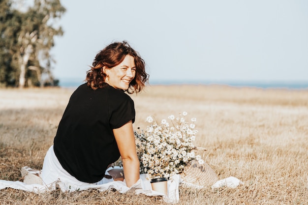 Retrato de uma linda mulher com um buquê de flores descansando sobre um tapete no campo