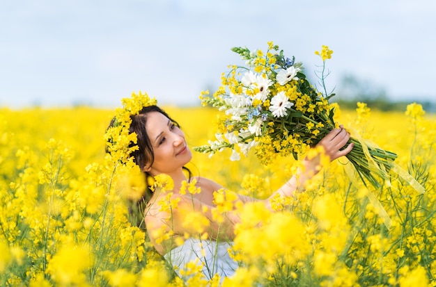 Retrato de uma linda mulher com uma coroa de flores amarelas na cabeça Uma garota com um buquê em um campo de colza