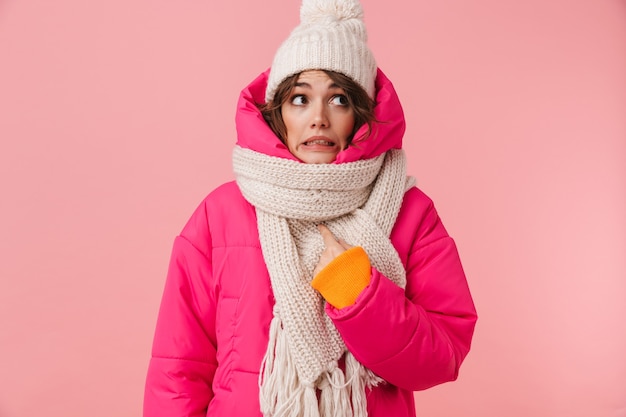 Retrato de uma linda mulher confusa em roupas quentes, apontando o dedo para si mesma, isolada no rosa