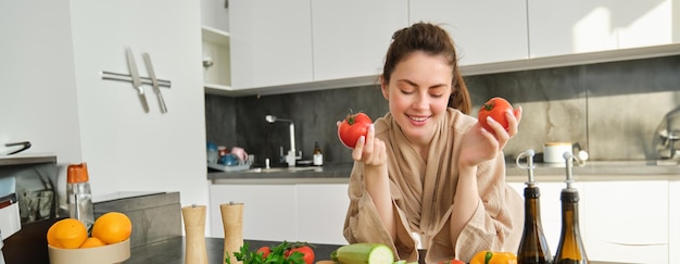 Retrato de uma linda mulher cozinhando na cozinha cortando legumes a bordo segurando tomates