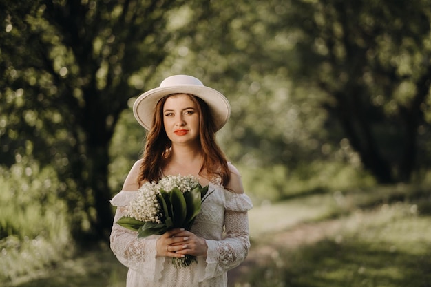 Retrato de uma linda mulher em um vestido branco e um chapéu com lírios do vale uma garota na natureza