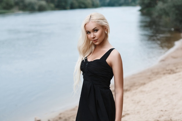 Retrato de uma linda mulher em um vestido preto na praia do rio