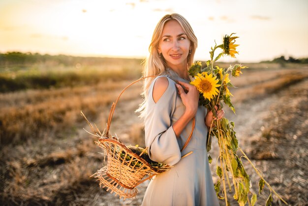 Retrato de uma linda mulher encantadora caminhando com uma cesta e girassóis nos braços