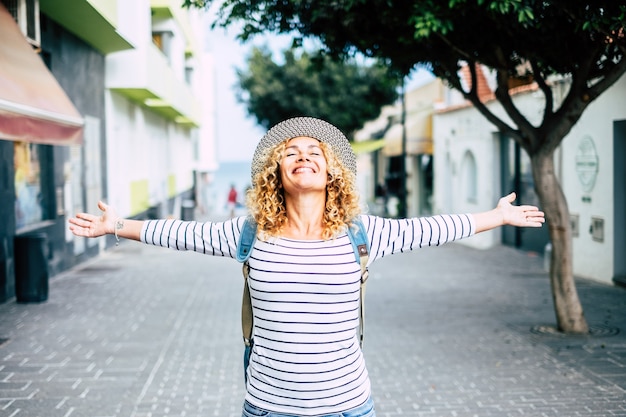 Retrato de uma linda mulher feliz com os braços abertos em sinal de liberdade no meio da rua sorrindo e curtindo - menina bonita encaracolada viajando ao redor do mundo se divertindo