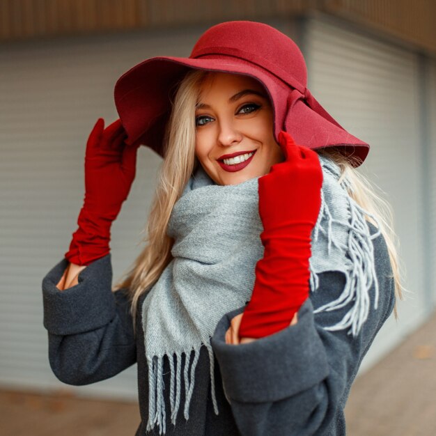 Retrato de uma linda mulher feliz com um sorriso em um chapéu da moda e um casaco cinza com um lenço cinza ao ar livre