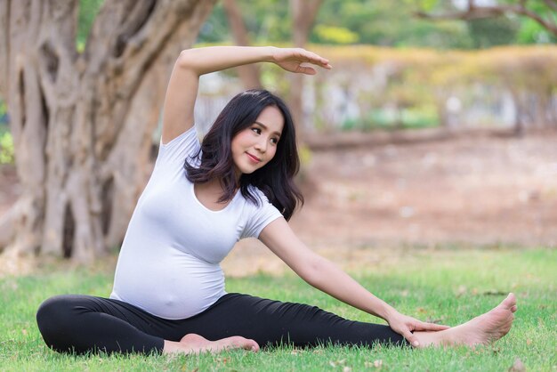 Retrato de uma linda mulher grávida asiática no parqueTailândia pessoasConceito de mulher felizEla joga ioga no gramado