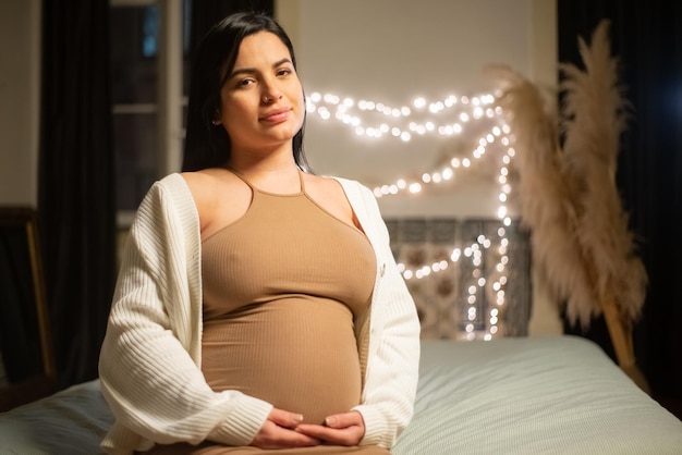 Retrato de uma linda mulher grávida. Mulher morena de vestido e casaco de lã tocando a barriga grande, olhando para a câmera. Gravidez, conceito de expectativa