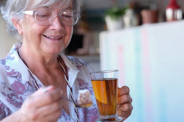 Retrato de uma linda mulher idosa em uma cafeteria, desfrutando de um chá de ervas e bolo de amêndoa