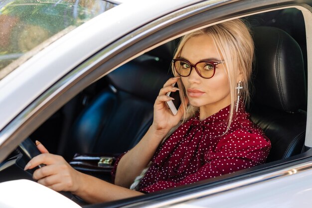 Retrato de uma linda mulher loira com um vestido vermelho, sentada em um carro com um telefone
