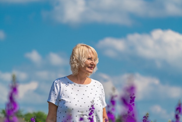 Foto retrato de uma linda mulher loira de meia-idade feliz em um campo com flores, fundo de céu azul