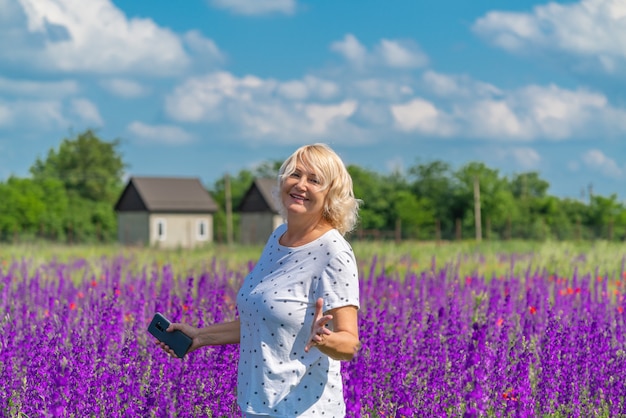 Foto retrato de uma linda mulher loira de meia-idade feliz em um campo com flores, fundo de céu azul