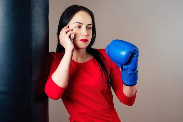 Retrato de uma linda mulher morena com luvas de boxe e um telefone nos braços no ginásio. atleta com boxe de batom vermelho de maquiagem. conceito de poder feminino, feminismo.