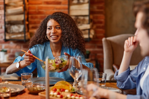 Foto retrato de uma linda mulher negra desfrutando de um jantar com amigos em um ambiente aconchegante