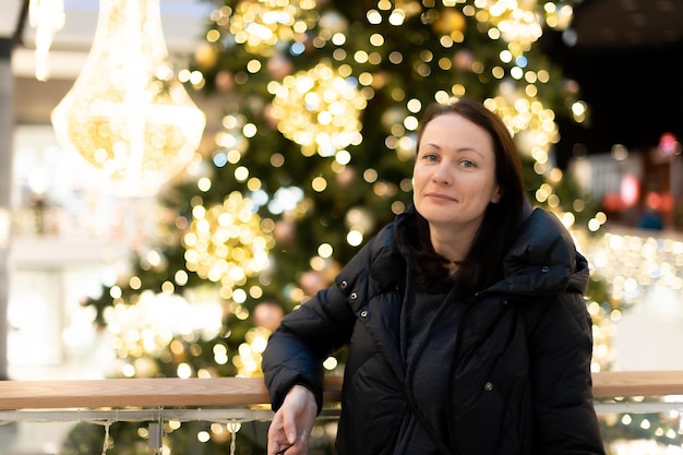 Retrato de uma linda mulher no fundo de uma árvore de Natal com luzes brilhantes gerlant Belo bokeh multicolorido ao fundo