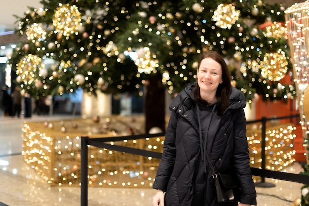 Retrato de uma linda mulher no fundo de uma árvore de Natal com luzes brilhantes gerlant Belo bokeh multicolorido ao fundo