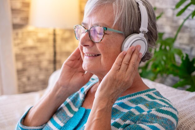 Retrato de uma linda mulher sênior com fones de ouvido sentado no sofá em casa ouvindo música com os olhos fechados