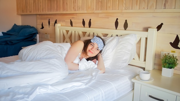 Retrato de uma linda mulher sorridente, deitada na cama em um quarto de hotel pela manhã