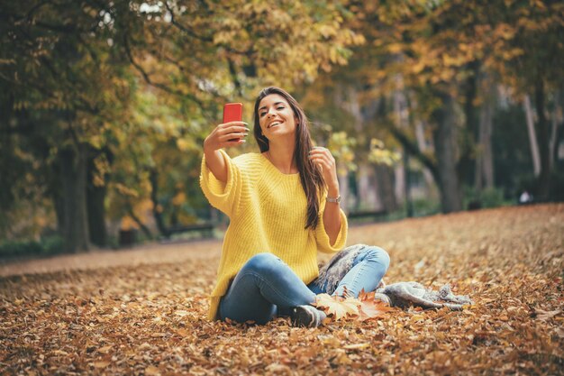 Retrato de uma linda mulher sorridente tomando selfie na floresta no outono.