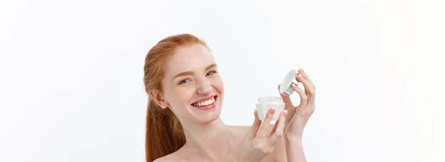 Retrato de uma linda mulher sorrindo enquanto toma um creme facial isolado em fundo branco com