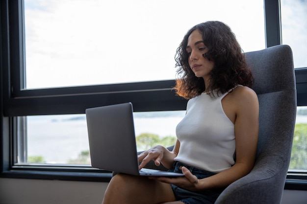 retrato de uma linda mulher sorrindo, sentada em uma poltrona com seu computador