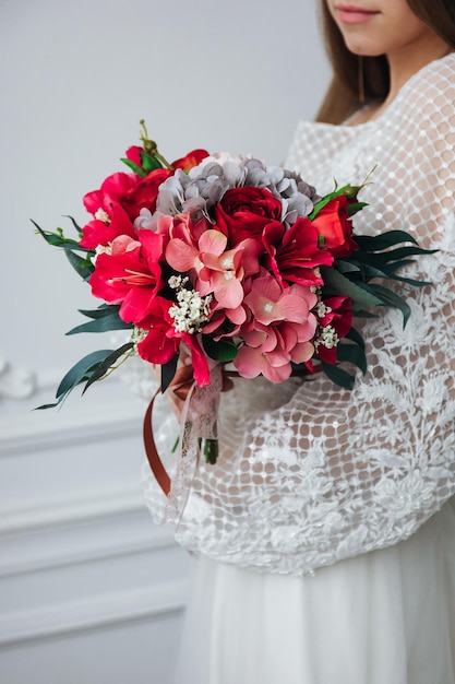 Foto retrato de uma linda noiva com um buquê de hortênsias e rosas vermelhas nas mãos em um interior leve