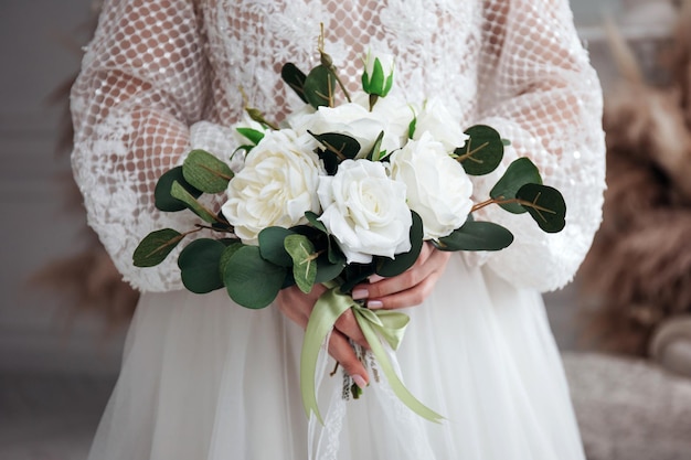 Retrato de uma linda noiva com um buquê de rosas brancas nas mãos em um interior leve