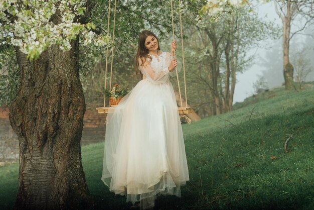 Retrato de uma linda noiva em vestido de noiva branco sorrindo e balançando na floresta