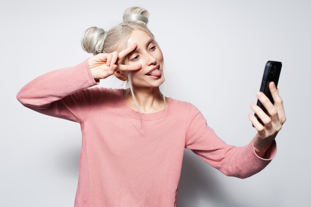 Retrato de uma loira atraente com pães de cabelo fazendo selfie no smartphone