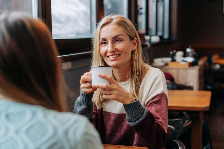 Foto retrato de uma loira atraente conversando com uma amiga enquanto estava sentada em um café aconchegante e quente