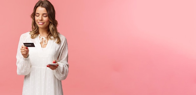 Retrato de uma loira atraente e fofa com vestido branco de penteado curto e encaracolado segurando smartphone