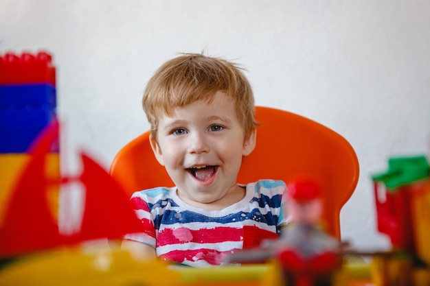 Retrato de uma loira rindo menino entre brinquedos de plástico coloridos brilhantes. Foto de alta qualidade