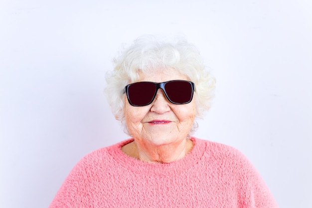 Retrato de uma loira sênior engraçada em óculos de sol e suéter rosa em fundo branco
