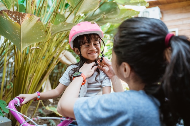 Retrato de uma mãe ajudando a filha usando um capacete antes de andar de bicicleta