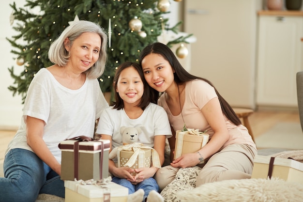 Retrato de uma mãe asiática feliz com suas duas filhas sorrindo, sentadas no chão, comemorando o Natal juntas