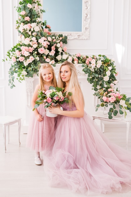 Retrato de uma mãe e filha em vestidos elegantes em um belo interior com flores.