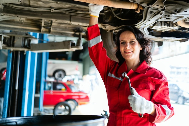 Foto retrato de uma mecânica caucasiana em um uniforme vermelho de pé sob o fundo do carro