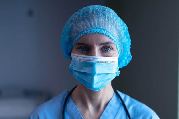 Retrato de uma médica caucasiana no hospital usando máscara facial, boné médico e jaleco