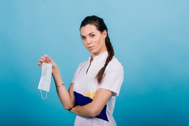 Retrato de uma médica com uma máscara médica, olhando para longe, isolada no azul