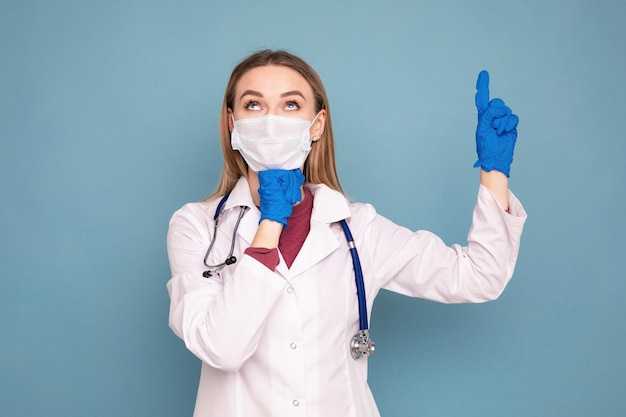 Retrato de uma médica em um jaleco branco e uma máscara médica Retrato emocional em um fundo azul isolado