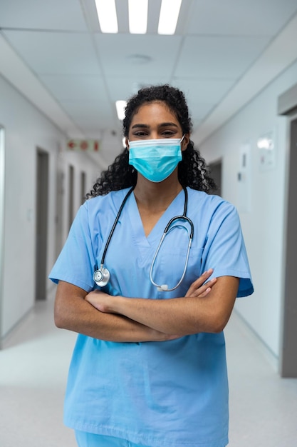 Retrato de uma médica mestiça usando máscara facial em pé no corredor do hospital