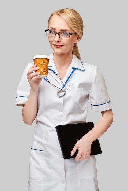 Retrato de uma médica segurando uma xícara de café de papel e segurando o tablet pc pad