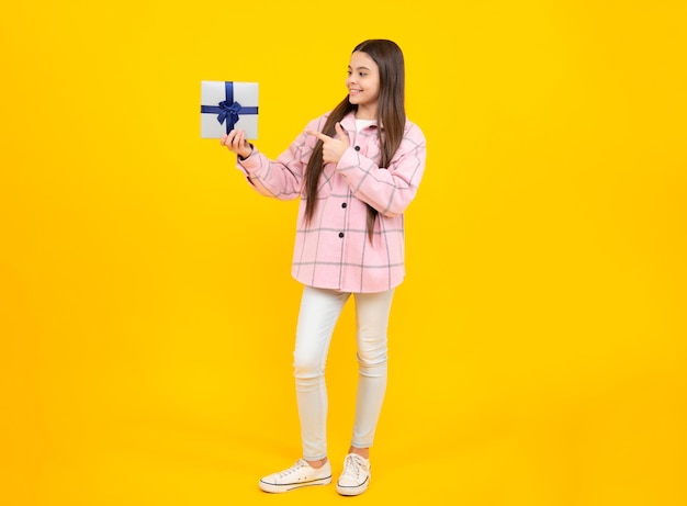 Retrato de uma menina adolescente segurando a caixa de presente isolada sobre o fundo amarelo do estúdio Conceito de saudação e presente de presente Conceito de feriado de aniversário