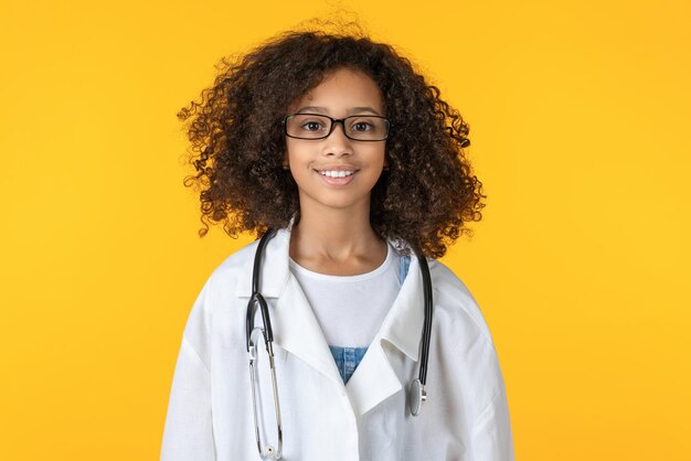 Retrato de uma menina africana bonitinha vestida como médico isolado em fundo amarelo