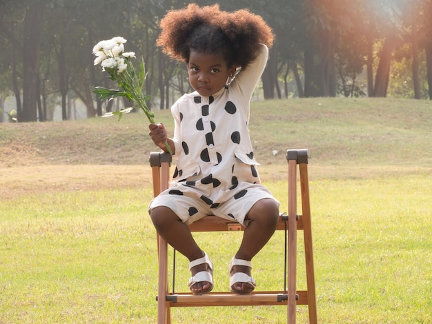 Retrato de uma menina afro-americana sentada na cadeira no jardim na bela manhã