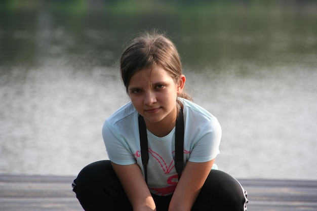 Foto retrato de uma menina agachada contra o lago